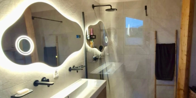 Finitions soignées pour une salle de bain moderne en Valais. Rénovation de salle de bain à Nendaz avec carrelage mural grand format et miroir design rétroéclairé.